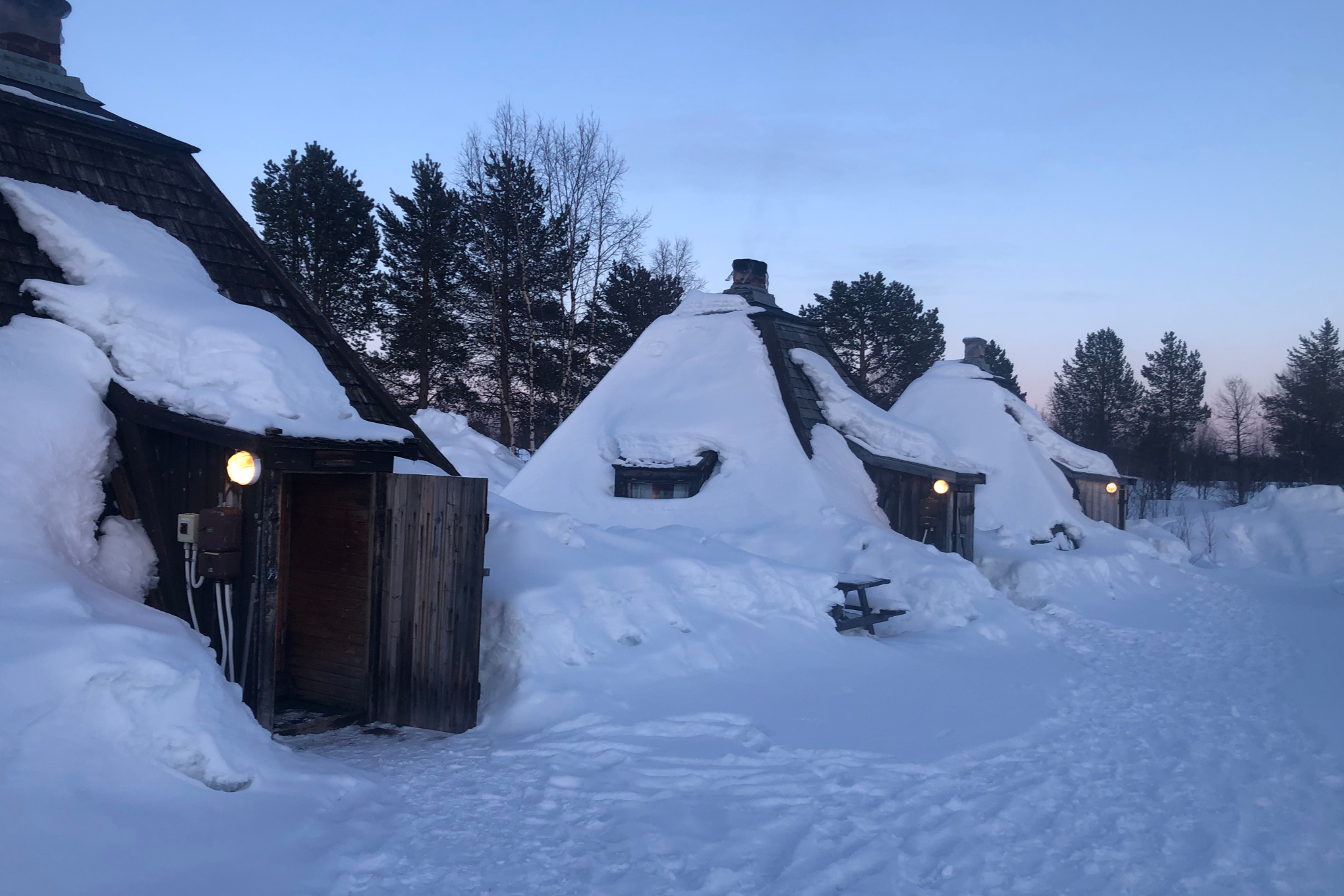 Snow-covered wilderness camp huts at dusk.